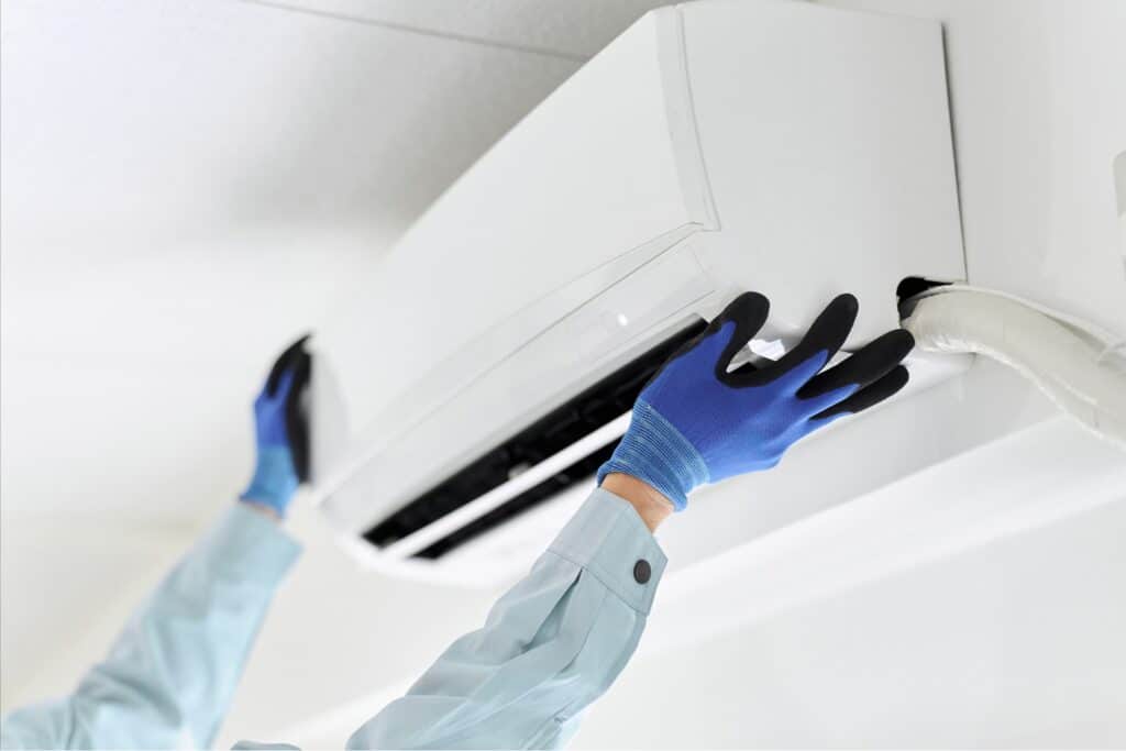 Technician with blue gloves installs an air conditioning system on the wall.