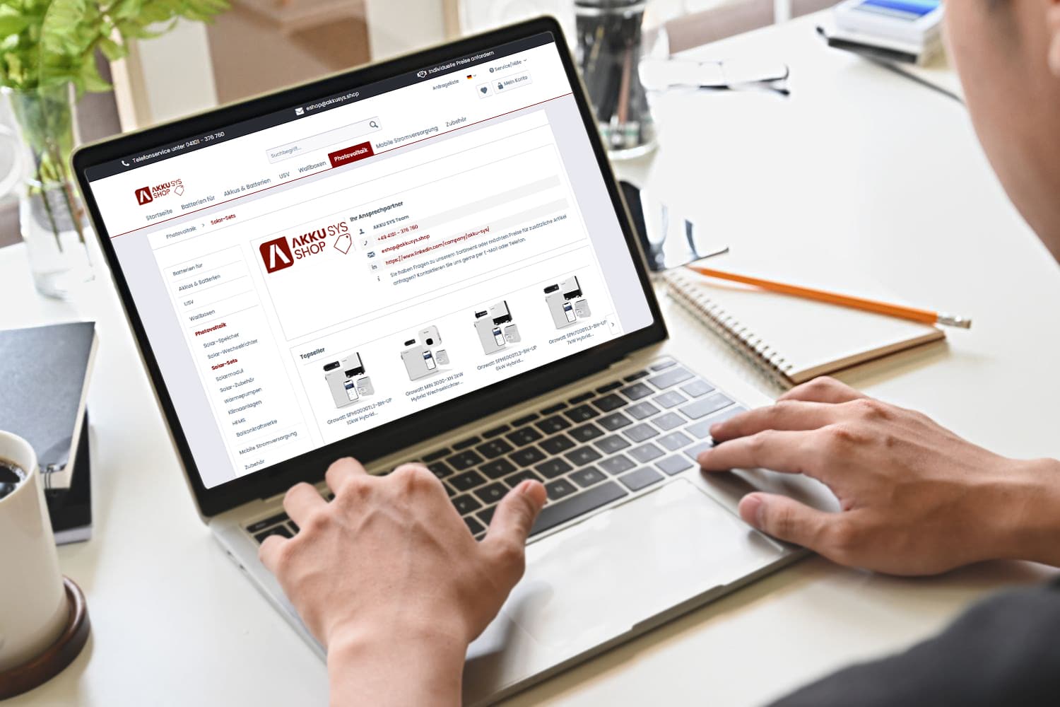 Person uses a laptop and visits the AKKU SYS online shop. The screen shows various products for mobile power supplies and photovoltaic components.