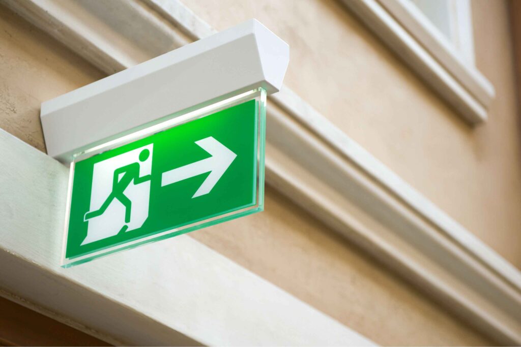 Green emergency exit sign on a beige wall with white frame