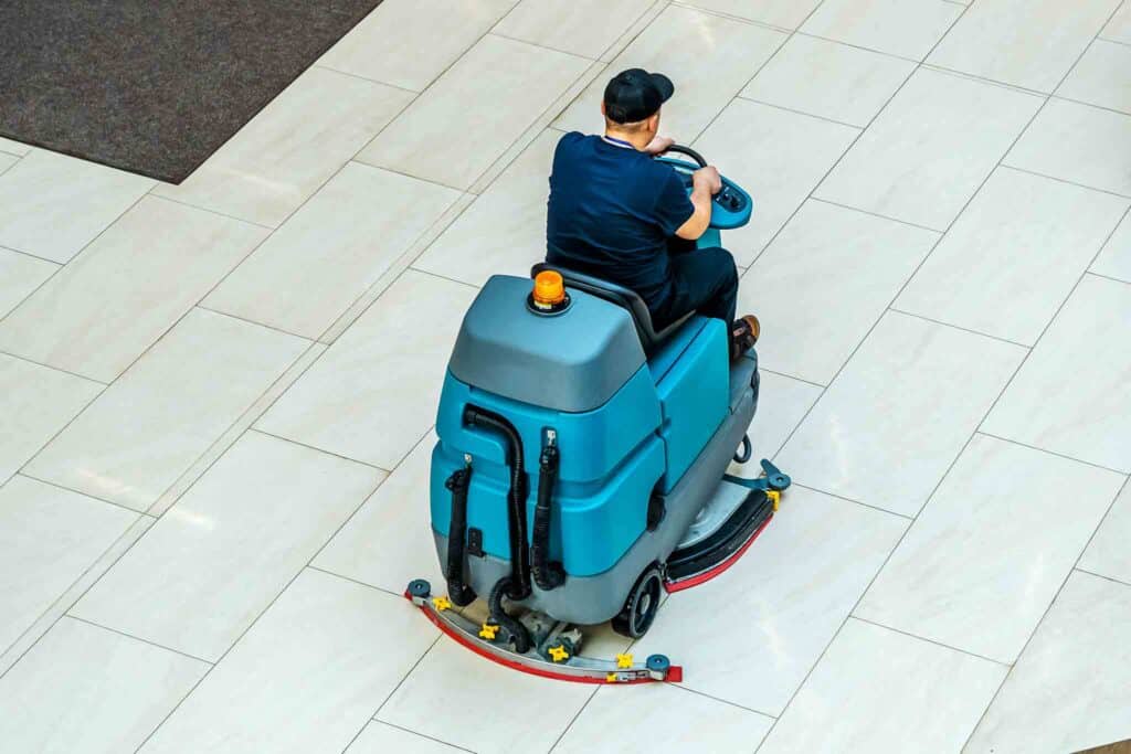 Blue cleaning machine with driver on a white floor.