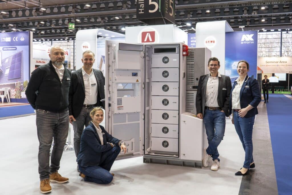 Team photo at the trade fair in front of an open SAJ CHS2 commercial storage unit. Five people pose smiling next to the storage unit on display, with the AKKU SYS stand in the background.