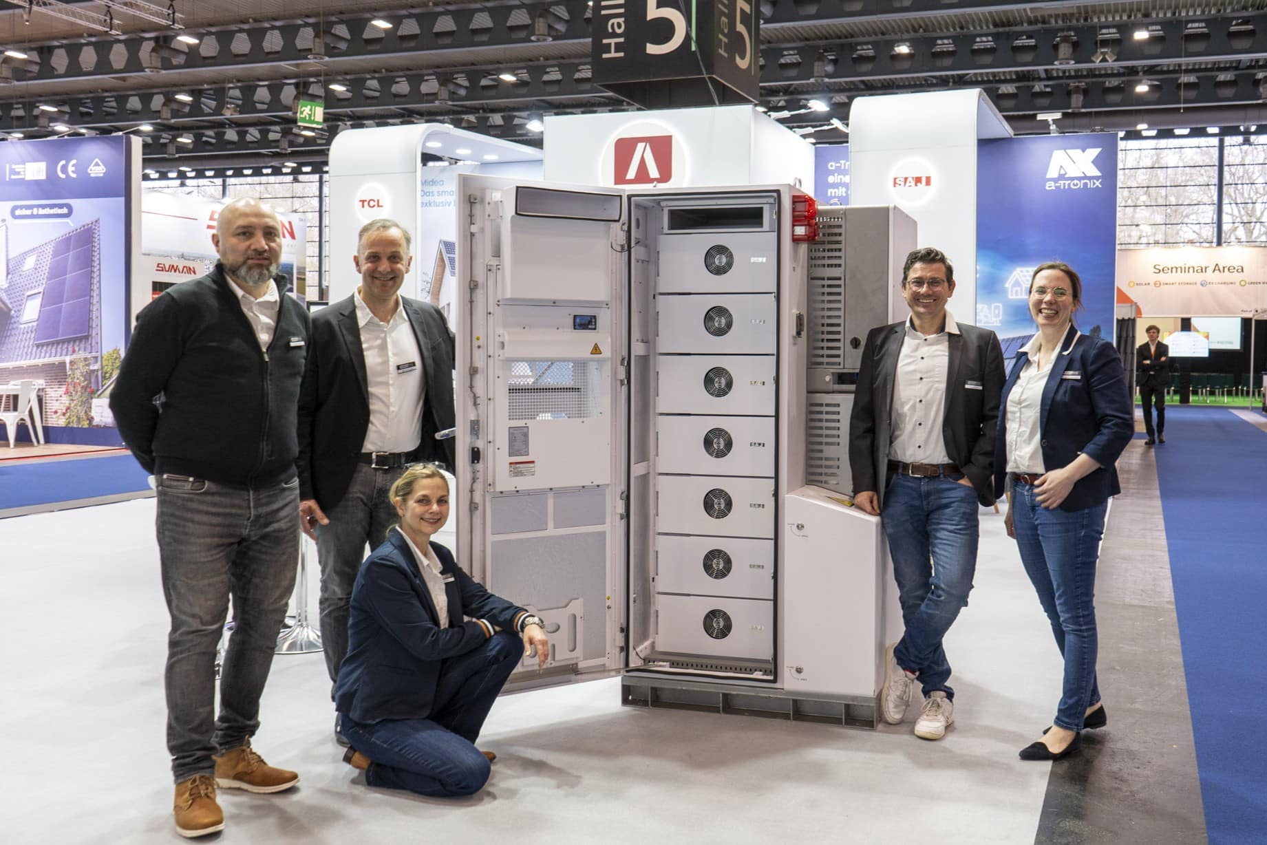 Team photo at the trade fair in front of an open SAJ CHS2 commercial storage unit. Five people pose smiling next to the storage unit on display, with the AKKU SYS stand in the background.