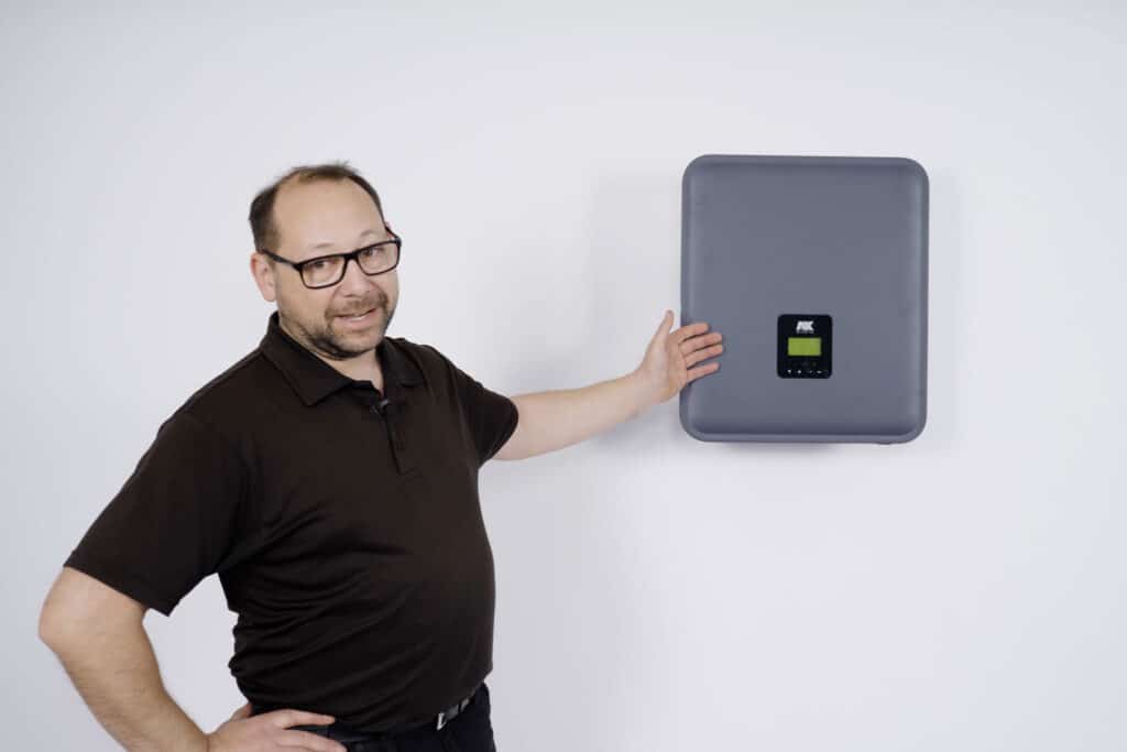 A trainer in black clothing points to a dark grey a-TroniX inverter as he explains.