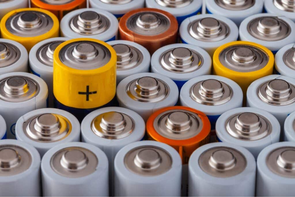 Close-up of various household batteries (type AA and AAA) with focus on the positive terminals in different colours.