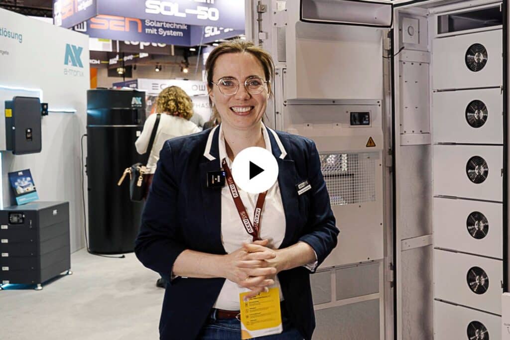 Eva Prumbohm from AKKU SYS stands in front of the SAJ CHS2 commercial storage unit. A play symbol in front of it.