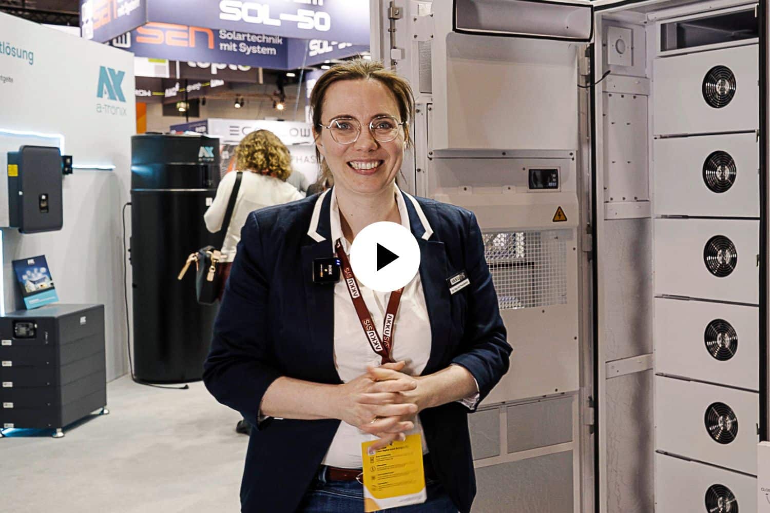 Eva Prumbohm from AKKU SYS stands in front of the SAJ CHS2 commercial storage unit. A play symbol in front of it.