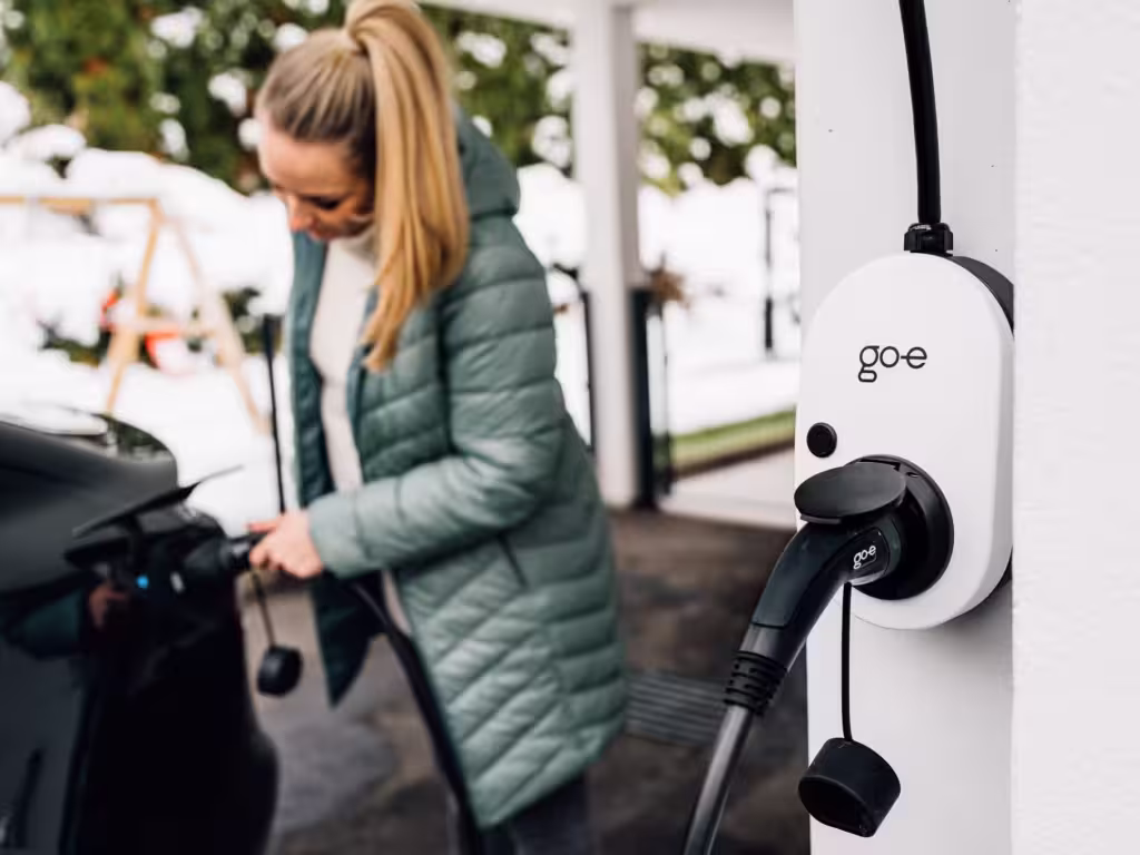 Woman with a green coat charges her electric car with a Go-e-Wallbox